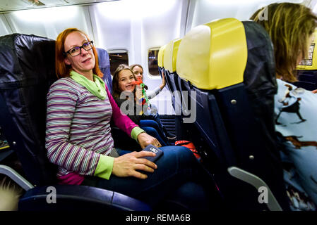 Famiglia seduti sui sedili in pelle in aeromobili commerciali. La madre e le figlie sono seduti su un basso costo compagnie aeree jet del passeggero aereo. Foto Stock