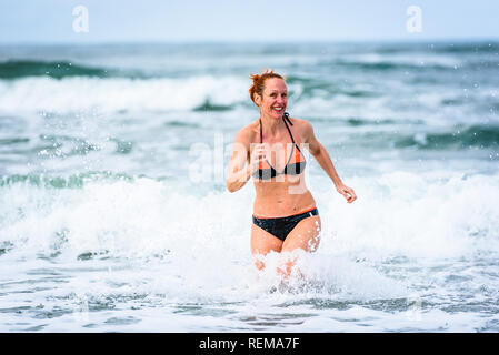 Donna godersi il mare e le onde dell oceano Atlantico. Matura, metà di età, giovane donna attraente in costume da bagno bikini è in esecuzione nell'oceano mare, playi Foto Stock