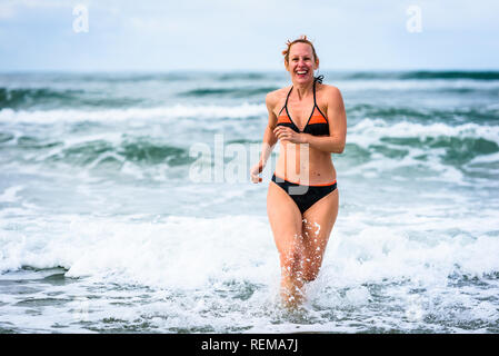 Donna godersi il mare e le onde dell oceano Atlantico. Matura, metà di età, giovane donna attraente in costume da bagno bikini è in esecuzione nell'oceano mare, playi Foto Stock