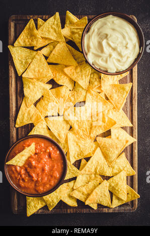 Nachos corn chips con pomodoro piccante e formaggio salse. Cibo messicano concetto. Mais giallo totopos chips con salsa di salsa. Vista dall'alto. Foto Stock