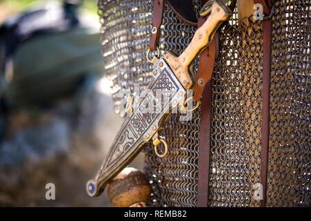 Argento o bronzo pugnale medievale con ornamenti attaccato alla catena armature, appeso nella striscia di cuoio. Soldati pronti per la battaglia. Rievocazione storica festival a Foto Stock