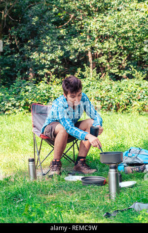 Trascorrere una vacanza in campeggio. Giovane uomo preparare un pasto all'aperto accanto alla tenda Foto Stock