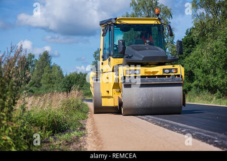 Giallo pesante vibrazione rullo in asfalto opere. Riparazione stradale in città. Strada in costruzione i lavoratori riparazione highway road sulla soleggiata giornata estiva. Foto Stock