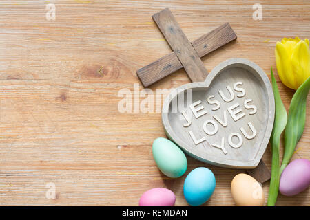 Croce di Pasqua e di cuore con iscrizione Gesù vi ama in legno astratto bordo della molla Foto Stock