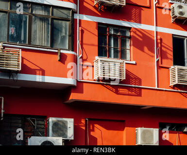 Bianco condizionatore aria condensatori due unità, uno piccolo e uno grande, installato sulla parete di cemento vicino alla finestra e tubo di acqua di edificio per uffici sfondo Foto Stock