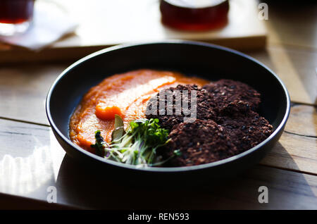 Vegano riso nero cotolette servita con arancia carote mesh e microgreeens e caffè decaffeinato. Cibo vegetariano hipster cafe. Foto Stock