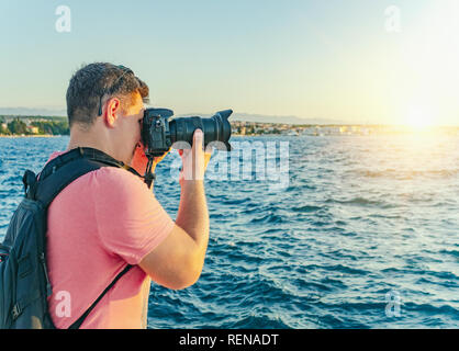 L'uomo con una telecamera a fotografare il tramonto sul mare. Foto Stock