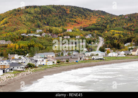 Gli alberi con i colori dell'autunno su una collina sulla penisola di Gaspé del Quebec, Canada. Case davanti la spiaggia. Foto Stock