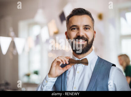 Un ritratto di un uomo maturo in piedi in ambienti chiusi su un party, azienda bowtie in legno. Foto Stock