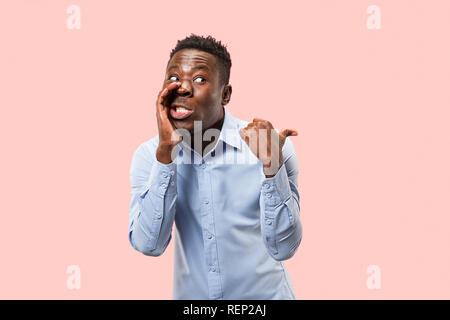 Secret, concetto di pettegolezzo. Giovane uomo afro sussurra un segreto dietro la sua mano. Imprenditore isolato sulla tendenza rosa di sfondo per studio. Giovane uomo emotivo. Le emozioni umane, espressione facciale concetto. Foto Stock