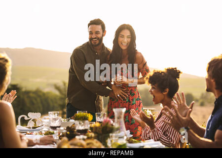 Felice coppia giovane annunciando la loro gravidanza a una festa. Uomo con la sua ragazza a sorpresa la condivisione di gravidanza annuncio con amici a cena Foto Stock