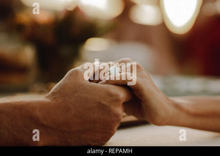Ritagliato colpo di giovane holding hands seduta a tavola. Coppia romantica seduti insieme. Foto Stock
