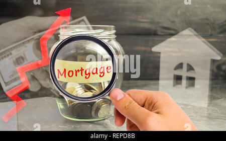 Vaso di vetro con monete e l'iscrizione di ipoteca ' ' e freccia verso l'alto. L'aumento dei tassi di interesse sui mutui. Mutui e Finanziamenti. Foto Stock