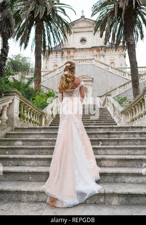 Grazioso sposa salite le scale di pietra in un abito da sposa Foto Stock