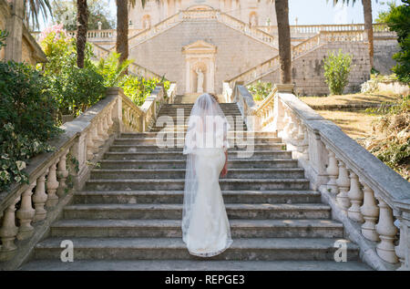 Grazioso sposa salite le scale di pietra in un abito da sposa Foto Stock