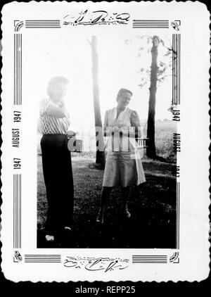 Due donne a riposare in un ambiente all'aperto tra alberi, in posa e sorridente, come una donna si prepara a prendere l'altra donna di fotografia con una Kodak Brownie box camera, Agosto 1947. () Foto Stock