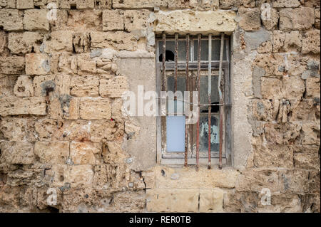 Vetro rotto con barre di ferro insieme in un vecchio muro di pietra calcarea. Foto Stock