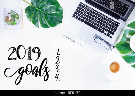 2019 Nuovo anni obiettivi - laici piana home office area di lavoro con computer portatile e foglie verdi monstera sulla scrivania bianca Foto Stock