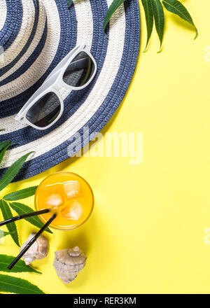 Viaggio estivo Concetto di vacanza. Striped hat, bere, occhiali da sole e foglie tropicali su sfondo giallo. Vista da sopra con copia spazio. Foto Stock