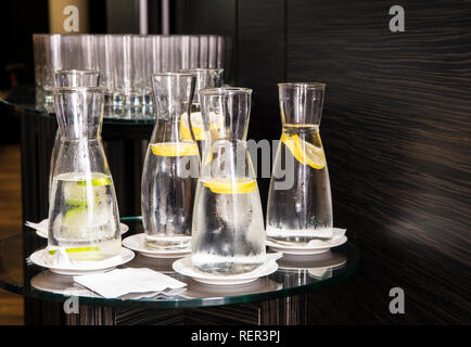 Molti caraffe trasparenti con acqua di limone su sfondo di legno. Foto Stock