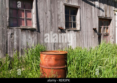 Grigio vecchio fienile in legno e arrugginita tamburo di petrolio Foto Stock