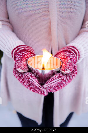 Il fuoco selettivo sulla donna che indossa guanti a maglia e maglione tenendo accesa una candela all'aperto(noto anche come torcia di passo o un giardino candela), all'aperto in w Foto Stock