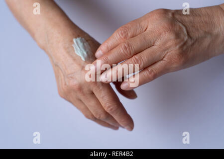 La cura della pelle. Donna anziana si applica la crema sulle mani. Prodotto di bellezza. Foto Stock