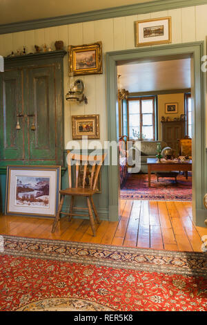 Vecchia sedia in legno nel salottino decorato con numerosi dipinti e la porta che conduce al soggiorno all'interno di un vecchio circa 1805 Canadiana stile home Foto Stock