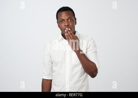 Scioccato giovane africano in abbigliamento formale che copre la bocca con la mano. Foto Stock