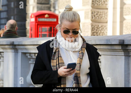 Gennaio 22, 2019 - Londra, Regno Unito - una donna è visto avvolto con una sciarpa mentre guardando il suo telefono cellulare in Westminster su un soleggiato ma freddo giorno nella capitale. Secondo il Met Office, si prevede che le temperature scendano al di -4C come ''pesanti acquazzoni neve'' coperta la nazione. (Credito Immagine: © Dinendra Haria/SOPA immagini via ZUMA filo) Foto Stock