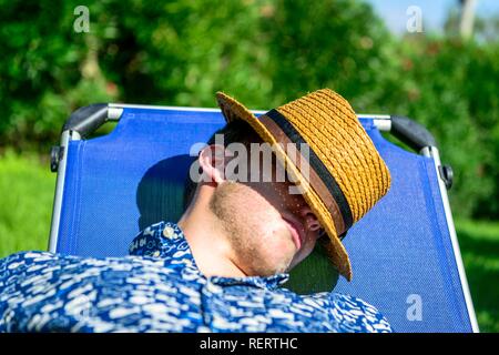 Giovane con un cappello di paglia di dormire su una sedia a sdraio in vacanza, Italia Foto Stock