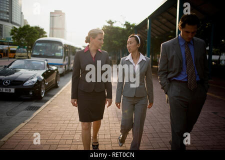 Tre colleghi di lavoro a piedi lungo la pavimentazione di una strada trafficata. Foto Stock