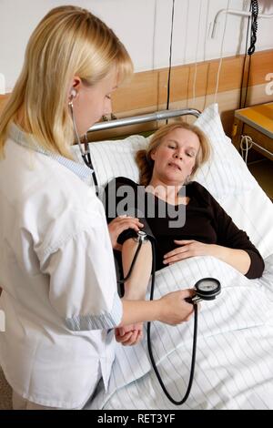 L'infermiera controllando la pressione del sangue di un paziente in un ospedale Foto Stock