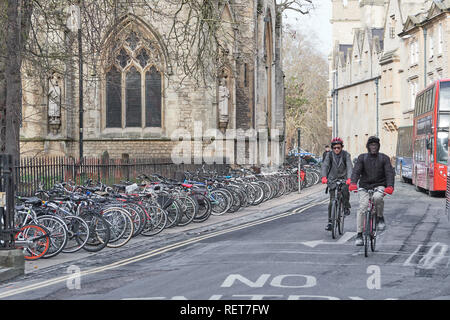 Due gli studenti di sesso maschile in bicicletta lungo il Magdalen Street East tra Balliol e biciclette parcheggiate in una fila ordinata al di fuori di Santa Maria Maddalena Foto Stock