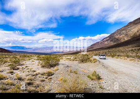 Viaggia su una strada sterrata attraverso una zona remota del Parco Nazionale della Valle della Morte; montagne, cielo blu e nuvole bianche in background; California Foto Stock