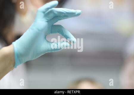 Medico dentista detiene il latte per neonati dente in mano e mostra che un piccolo paziente. Foto Stock