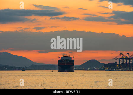 Uno scambi commerciali nave cargo spedizione dopo il tramonto da un porto commerciale Foto Stock