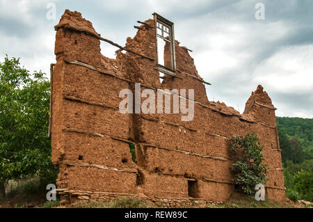 Muro di mattoni con adobe intonaco argilloso e legno rotti sul telaio di una finestra è rimasto rovinato il vecchio paese rurale casa su nuvoloso cielo blu sullo sfondo Foto Stock