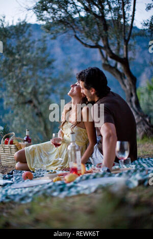 Giovane adulto giovane avente un picnic in un campo al tramonto. Foto Stock
