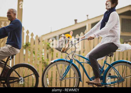 Uomo maturo e una giovane donna con il divertimento mentre in bicicletta attraverso una zona suburbana. Foto Stock