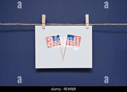 Due bandiere in miniatura di America USA sulla cartolina in bianco su sfondo blu appeso con clothespins. Biglietto di auguri per la celebrazione del Giorno del Presidente in Foto Stock