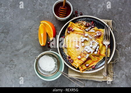 Flat-lay di crepes e rabboccato con melograno e lo zucchero sulla piastra. In casa frittelle sottili, di miele e frutta Foto Stock