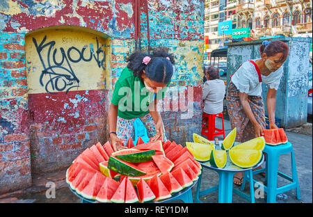 YANGON, MYANMAR - 17 febbraio 2018: i fornitori a stendere le fette di rosso e giallo cocomero, vendono nella strada malandato di Chinatown, su Februa Foto Stock