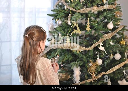 Bianco bambino caucasico, ragazza, in piedi con la schiena e decorare l'albero di Natale Foto Stock