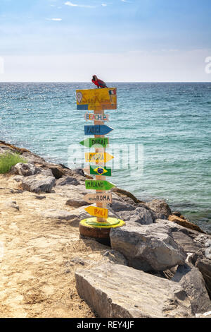 Polo colorata con le frecce che puntano a nomi di località in tutto il mondo, sulla spiaggia di San Remo in Italia Foto Stock