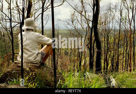 Uomo seduto su di una roccia e guardando le colline, Mia Mia la foresta di stato, Queensland, Australia Foto Stock