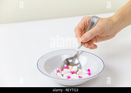 Dipendenza da farmaci e droghe in tempi moderni: la mano di una giovane donna con un cucchiaio di compresse presi da una piastra piena di medicinali sulla linguetta bianca Foto Stock