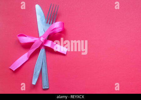 Cucchiaio con una forcella legate con un nastro su un sfondo rosa. Posate. Il giorno di San Valentino Foto Stock