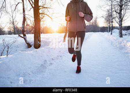 Donna attiva il jogging all'aperto in inverno. Persona di sesso femminile che corre lungo la strada innevata sulla bellissima giornata a freddo Foto Stock