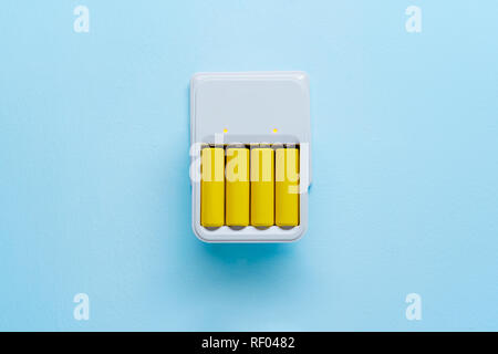 Foto di caricabatterie con batterie giallo vuota su sfondo blu Foto Stock